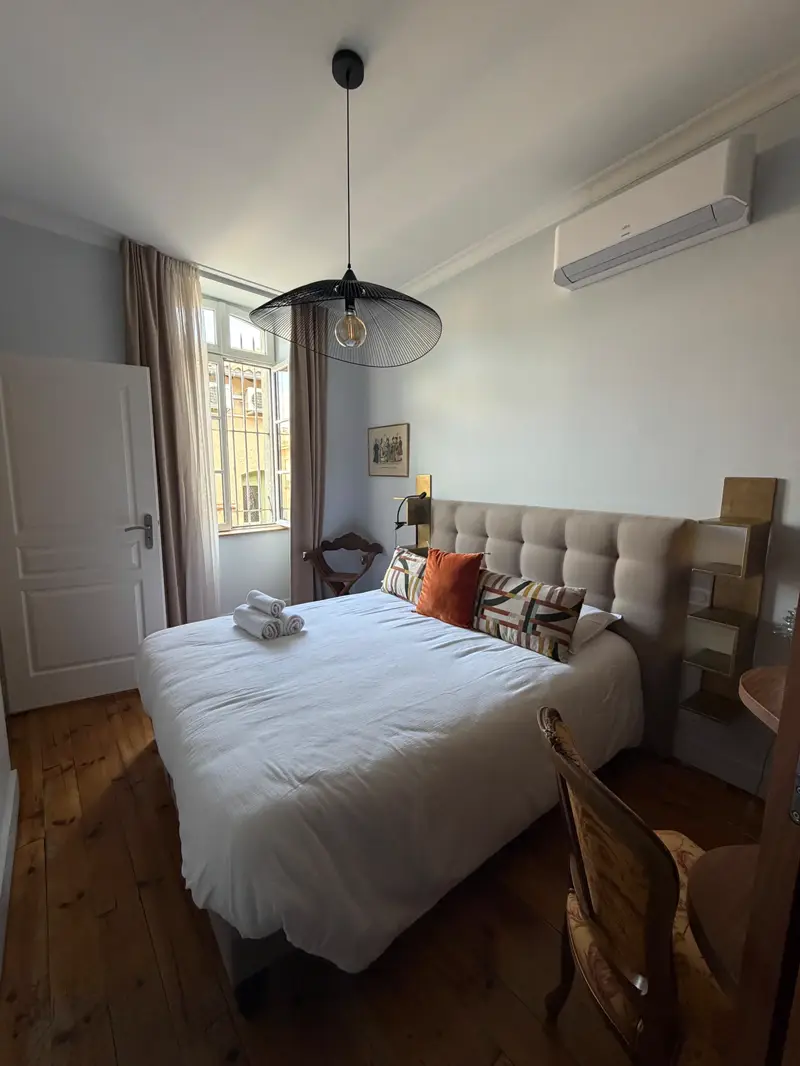 Chambre de l'appartement Apollon : lit double, tête de lit capitonnée, parquet ancien et fenêtre