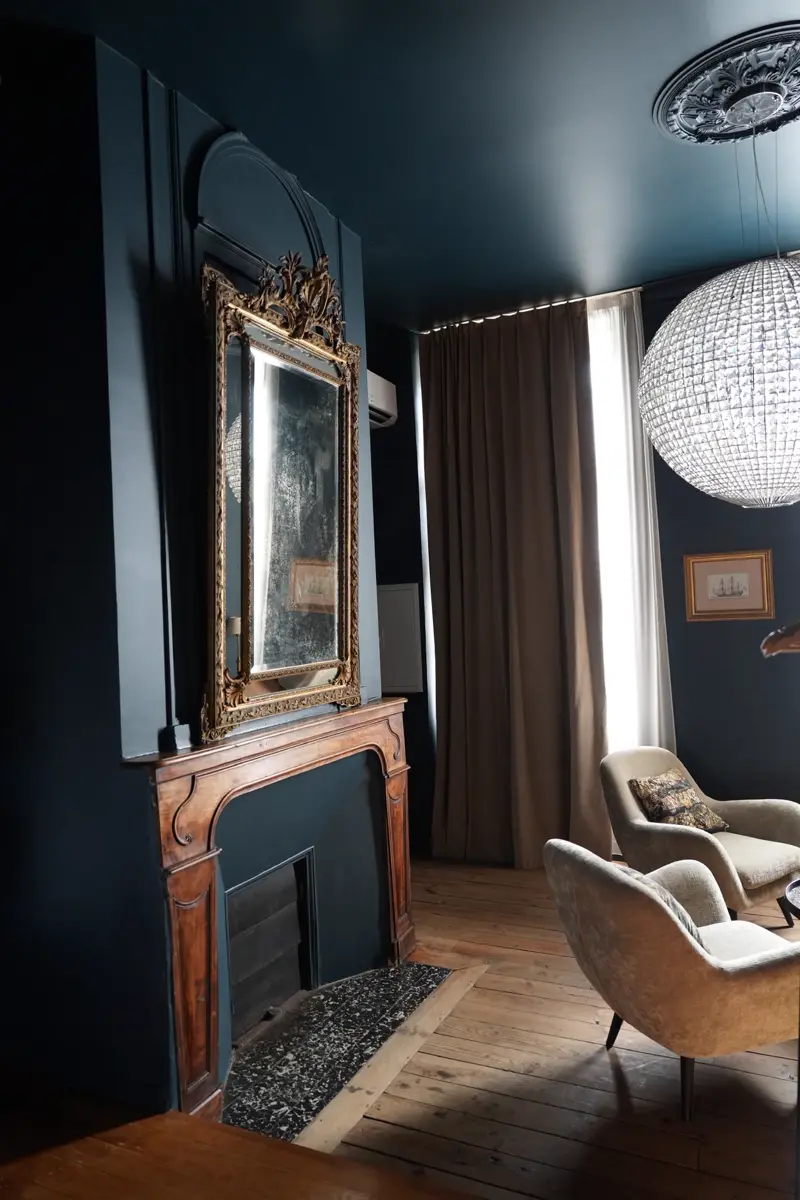 Cheminée en bois surmontée d'un miroir doré ancien, dans la chambre Louis XIV aux murs bleu nuit