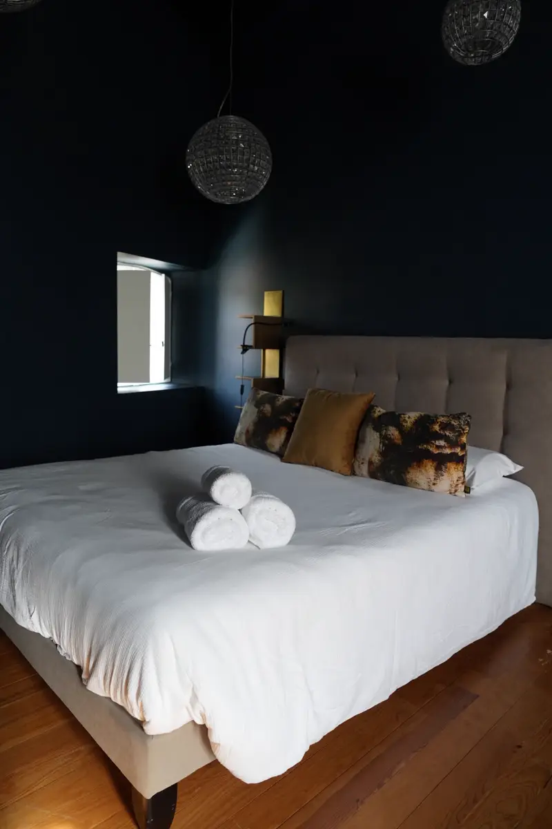 Grand lit de la chambre Louis XIV avec tête de lit capitonnée et coussins dorés sur murs bleu nuit