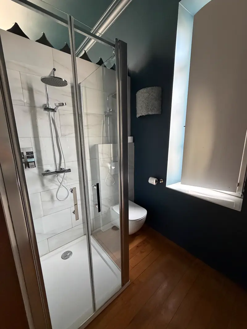 Salle d'eau de la chambre Louis XIV : cabine de douche en marbre blanc et WC suspendu