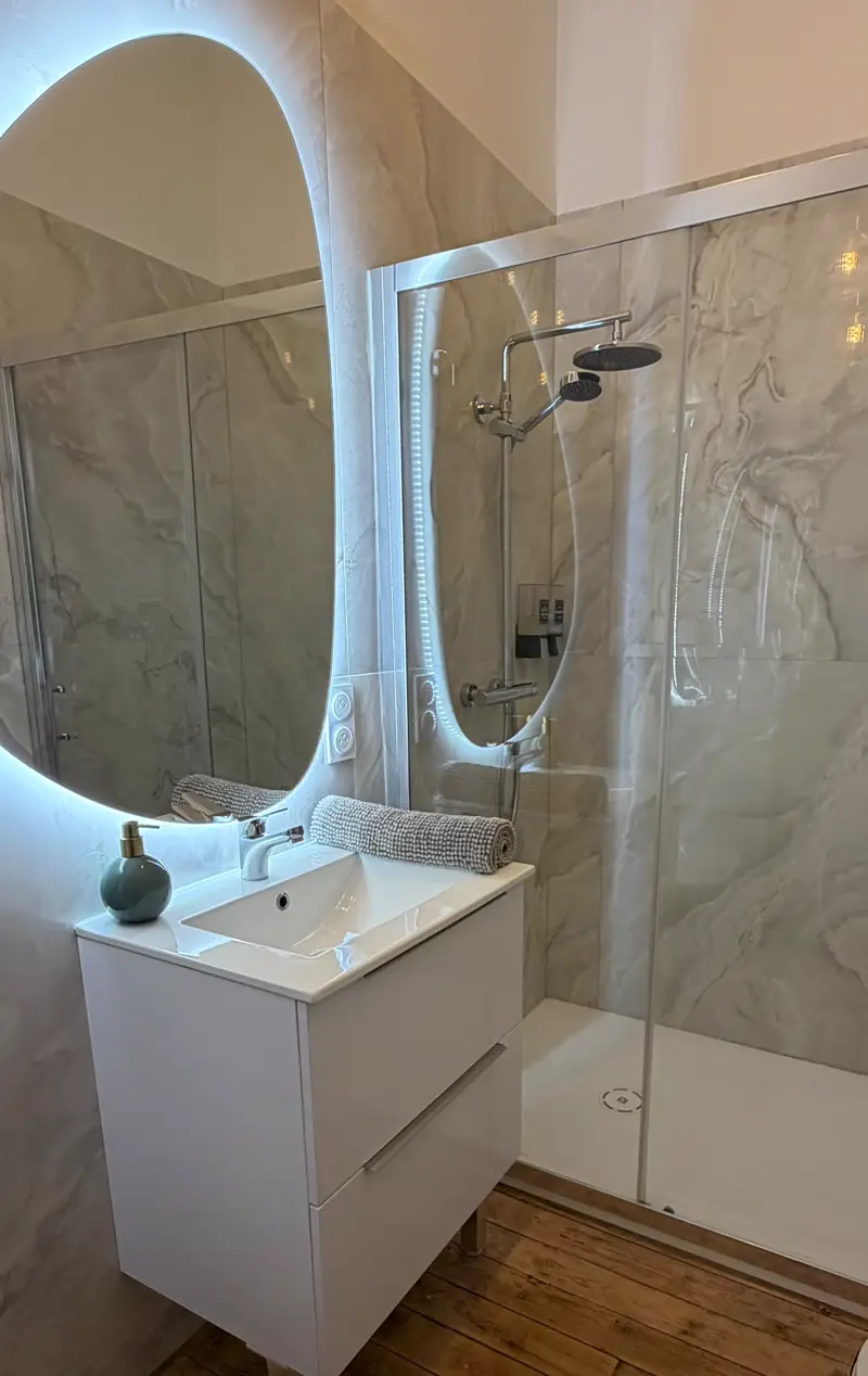 Salle de bain de l'appartement Mazarin : douche vitrée, meuble vasque blanc et miroir rétroéclairé