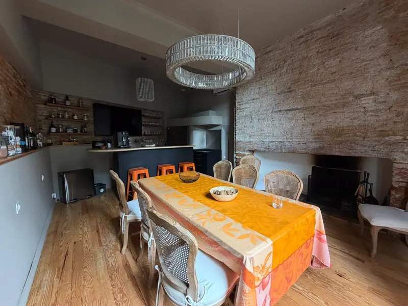 Salle commune de la Maison du Soleil : grande table dressée, bar, cheminée et mur de brique