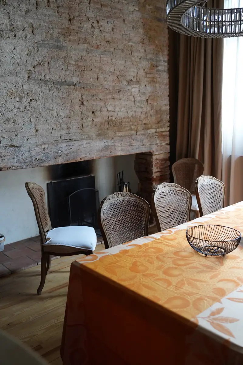 Grande table de la salle commune devant la cheminée et le mur de brique ancienne