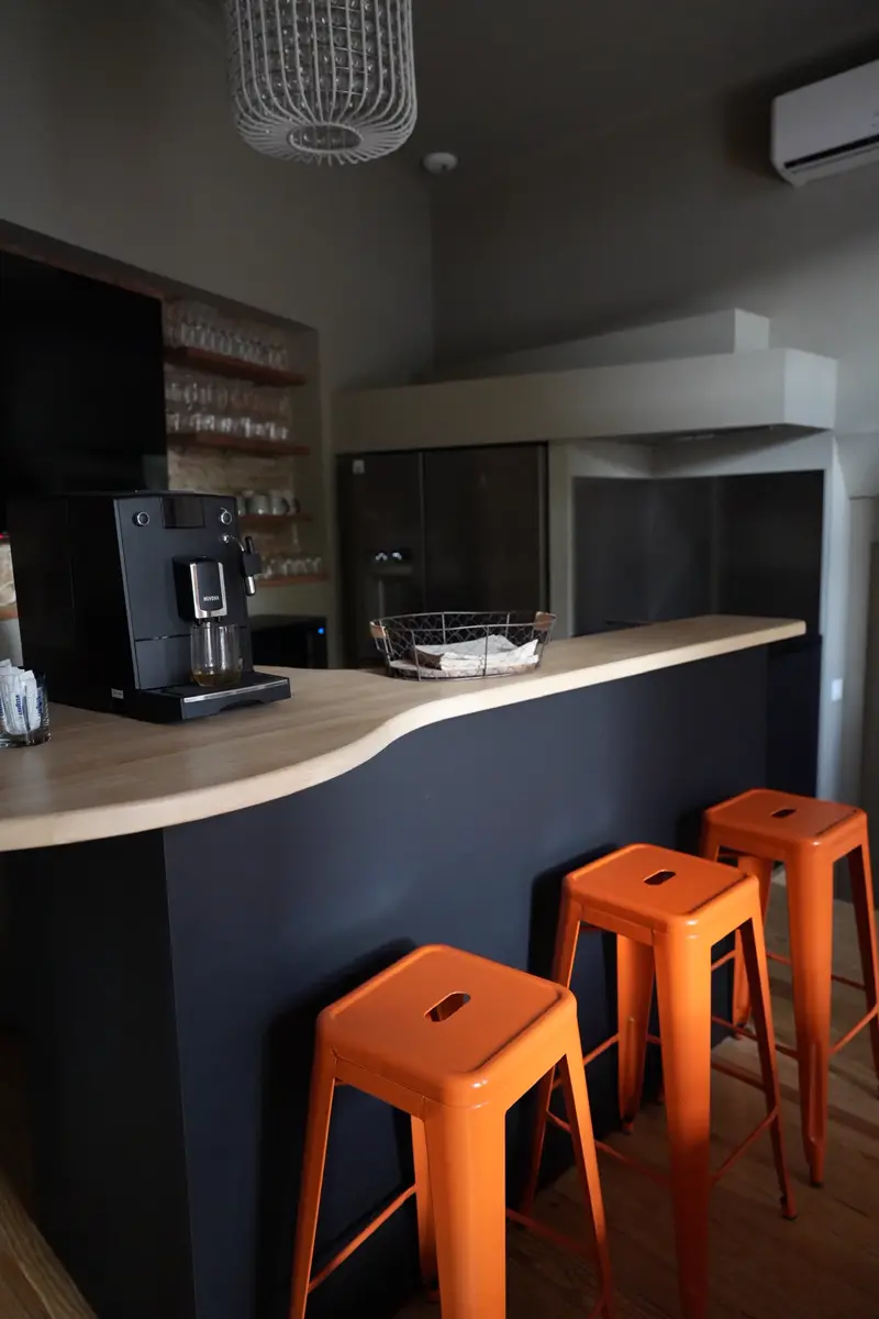 Bar en bois de la salle commune avec machine à café en libre service et tabourets orange